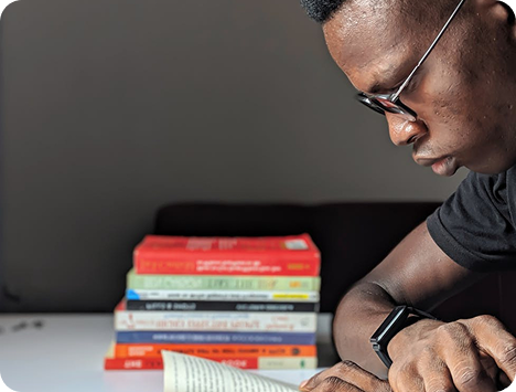Young man reading intently beside a stack of colorful books — representing 2Inspire Publications’ call to empower youth through focused, actionable learning.