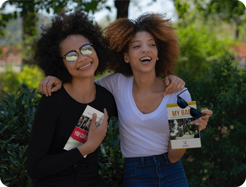 Two smiling young women outdoors, holding 2Inspire Publications guides ‘You Can Do It!’ and ‘My Bad’ — representing youth empowerment and personal growth.