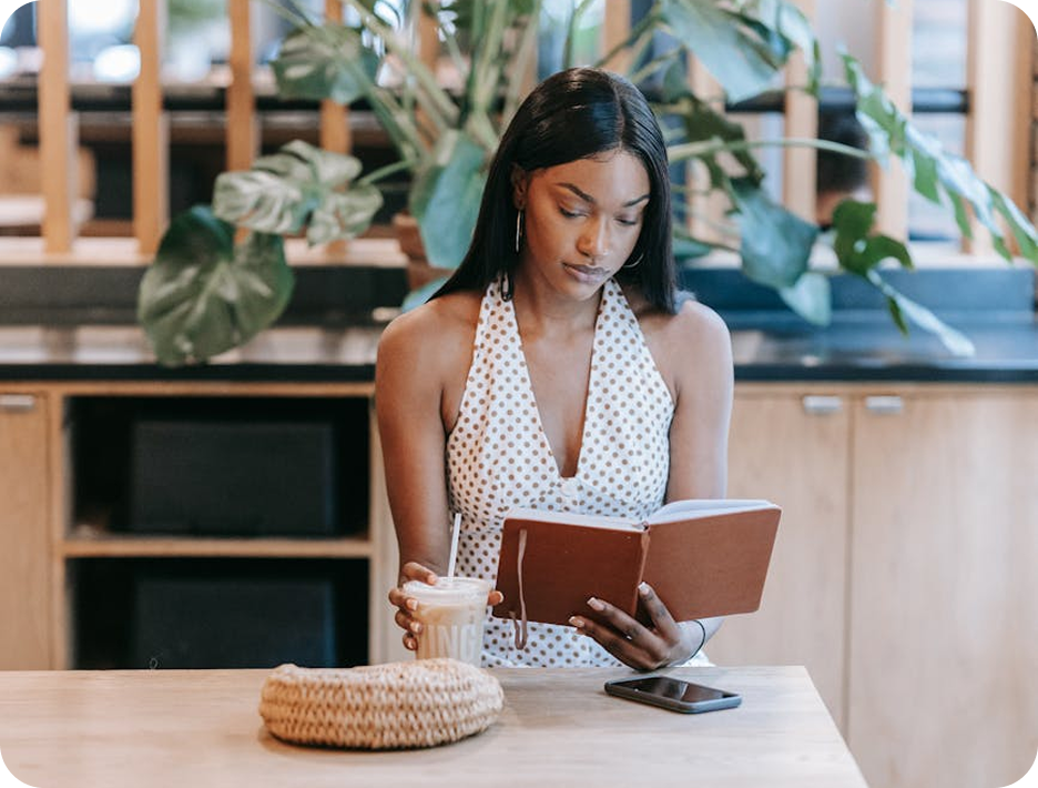 Young woman reading a journal in a cozy café, sipping iced coffee with focus and calm.