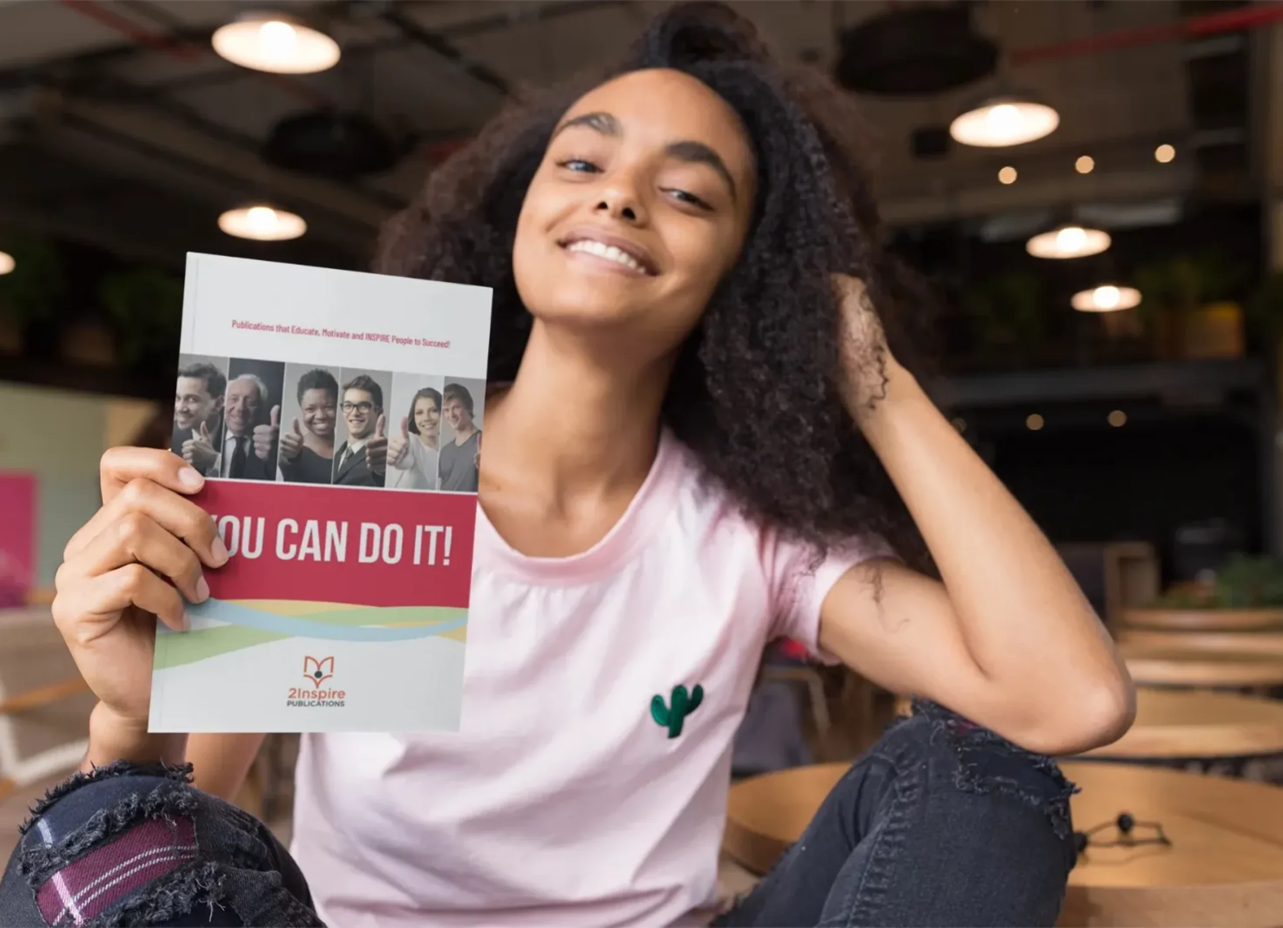 Confident young woman holding ‘You Can Do It!’ book from 2Inspire Publications, promoting youth empowerment and career development.
