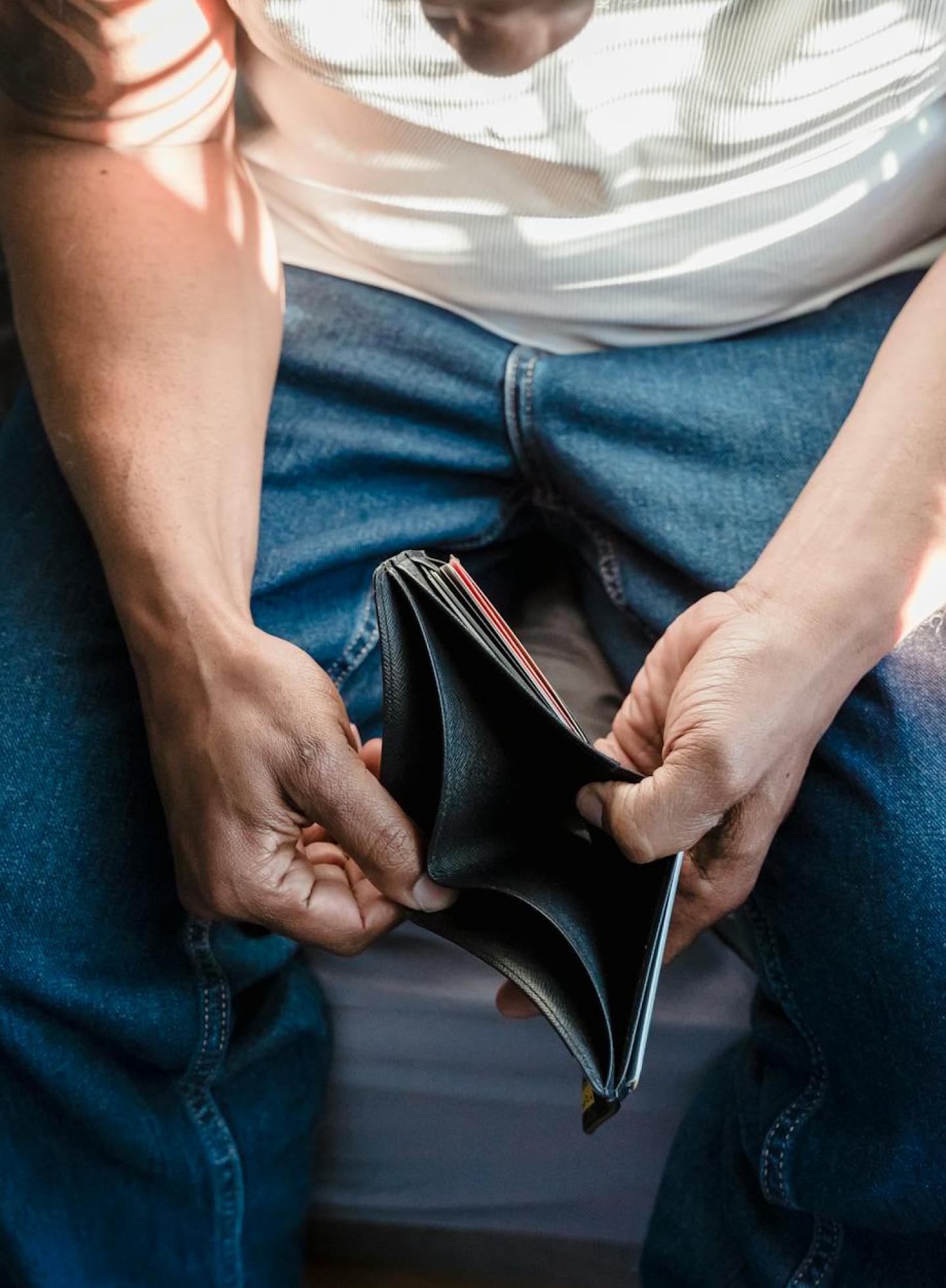 Man holding an empty wallet while seated, highlighting financial struggle and the importance of financial literacy.