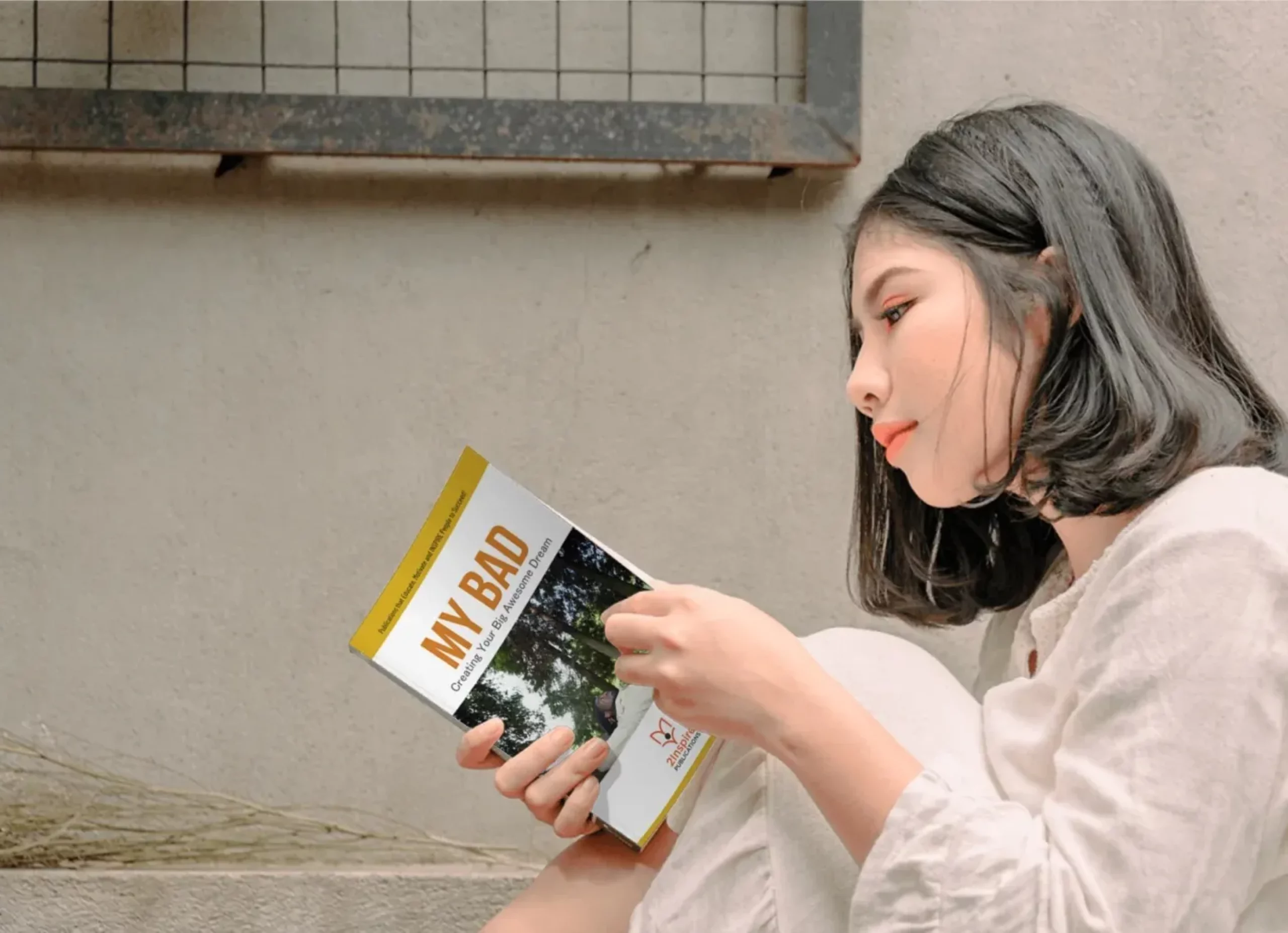 Young woman reading a personal growth booklet titled "My Bad" while sitting against a wall in deep reflection.